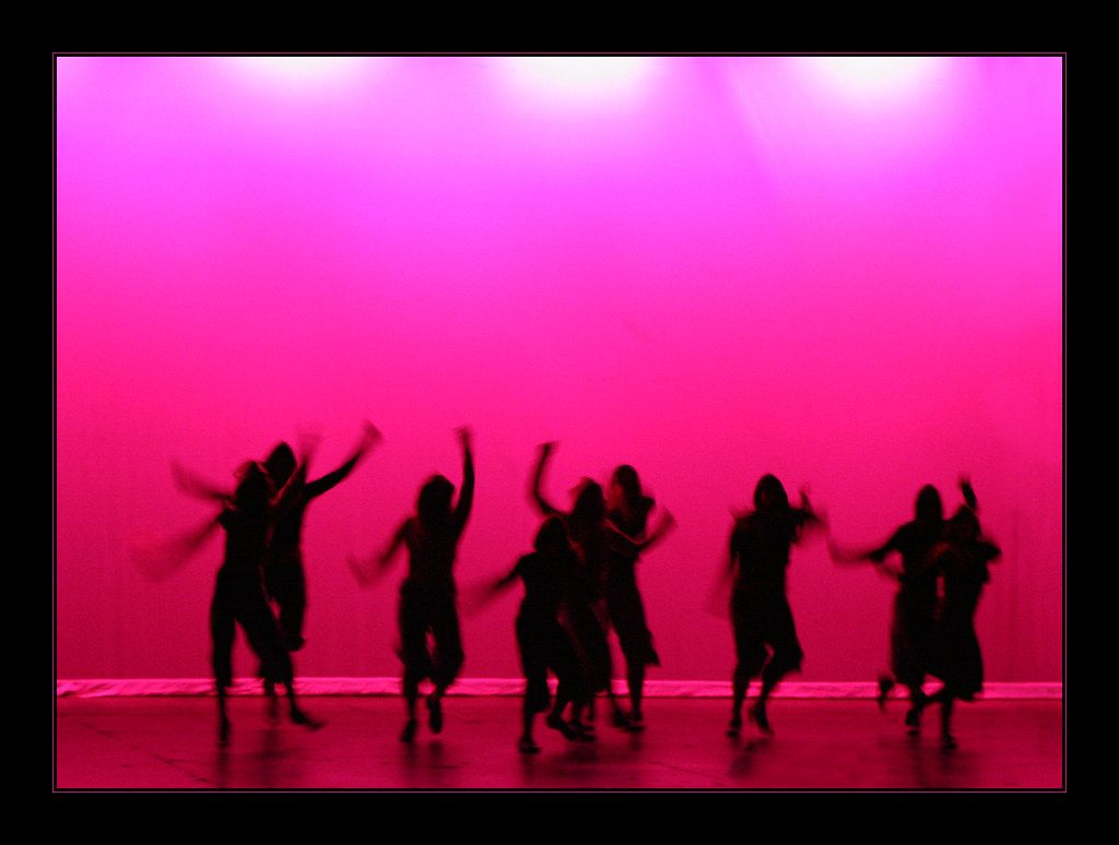 Silhouettes of dancers mid-move against a pink stage light